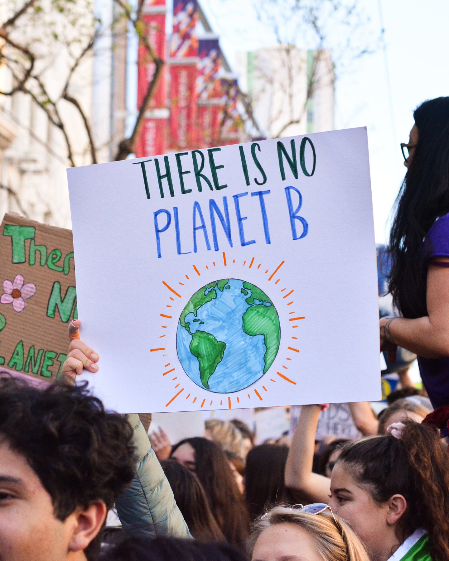 A sign is held up at an environmental protest. The sign reads "There is no Planet B" and has a drawing of the earth on it.