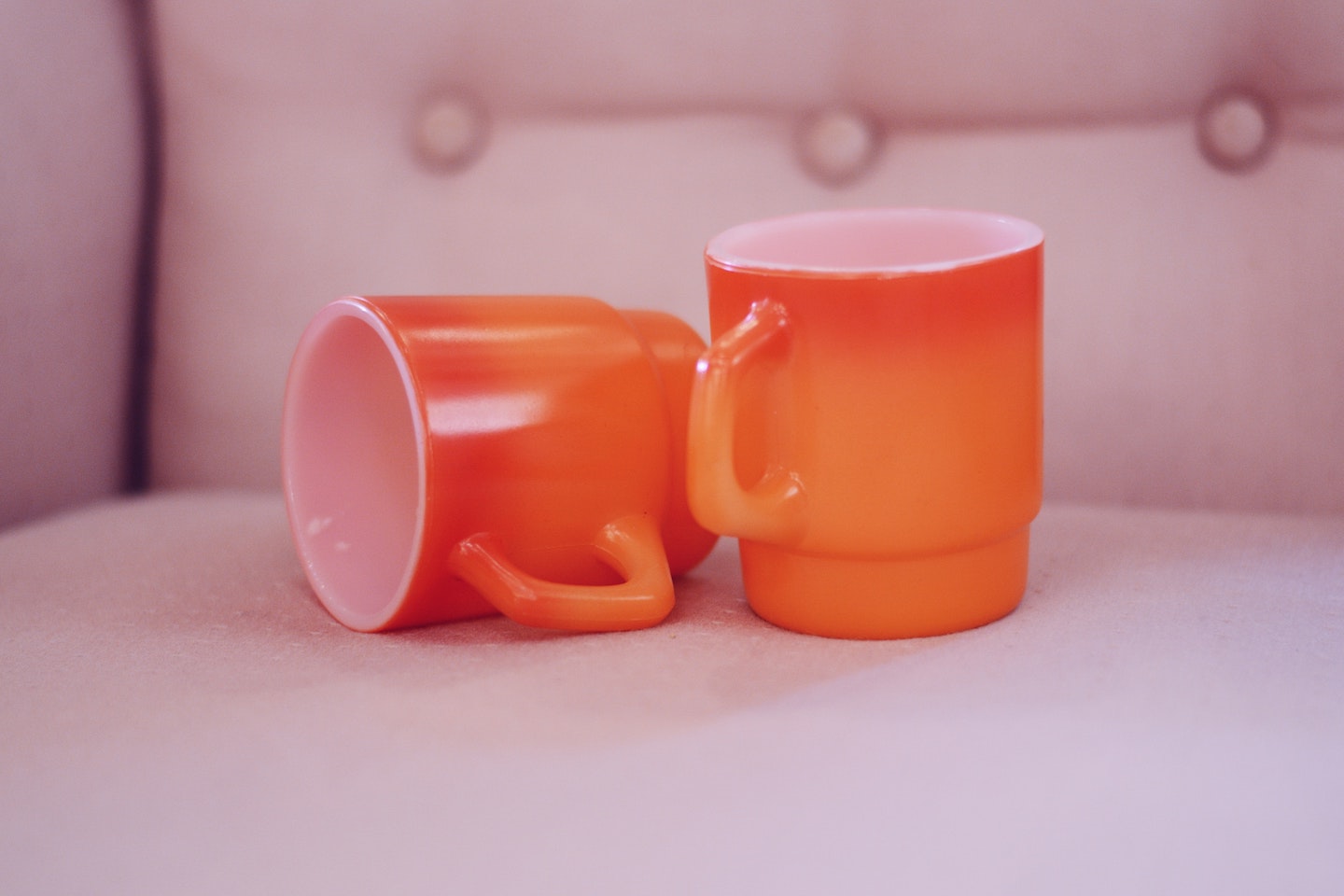 Two empty orange mugs are seen on a chair. One is laying sideways.