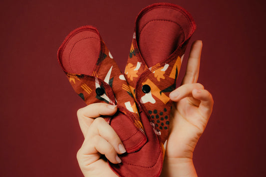 Two hands holding up a reusable aisle pad used for periods & bladder leaks