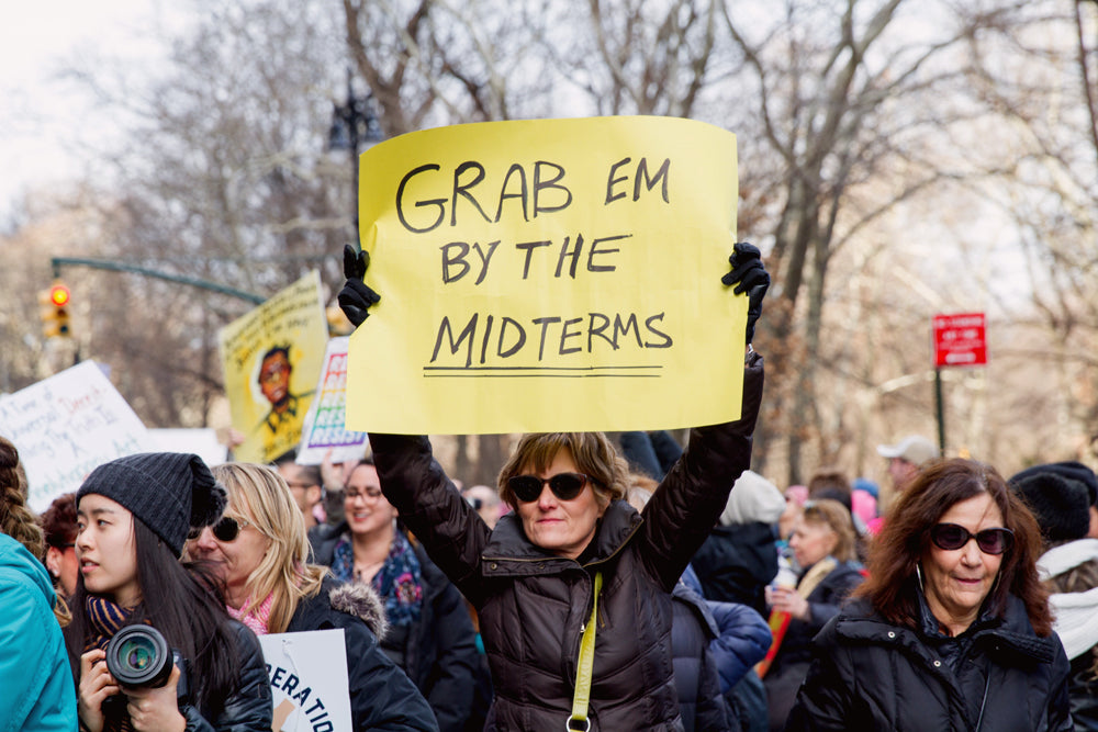 Woman at a protest holding up a sign that reads "Grab em by the midterms".