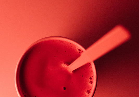 Red cup filled with a thick red liquid on a red background. There is a spoon standing in the cup.