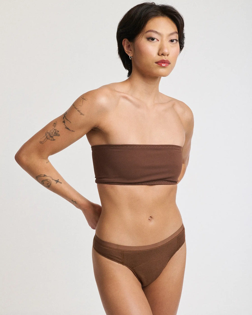 Front view of a woman wearing an Aisle Essential Thong period underwear in Espresso, with one arm bent | Espresso
